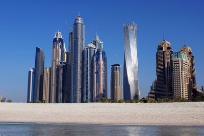 Low angle view of cayan tower by river against clear blue sky in city