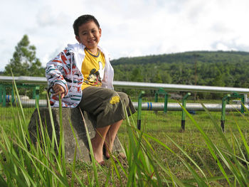 Portrait of boy sitting on stone at grassy field