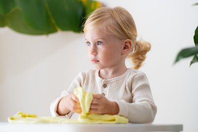 Portrait of cute girl playing with slime sitting on table