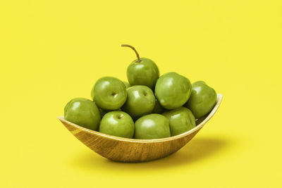 Green fruits in bowl against yellow background