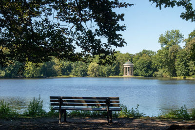 Bench in park by lake against sky