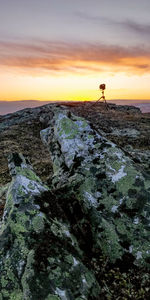 Man standing on rock by sea against sky during sunset