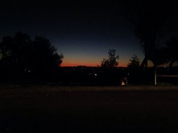 Silhouette trees on field against clear sky at night