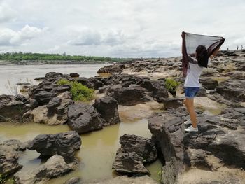 Woman standing on rock at beach against sky