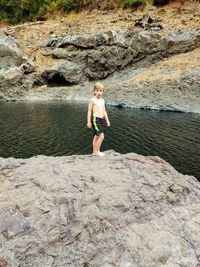 Full length of shirtless boy on rock at shore
