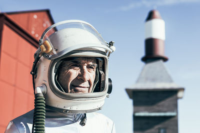 Full body man in spacesuit standing on rocky ground against striped rocket shaped antennas on sunny day