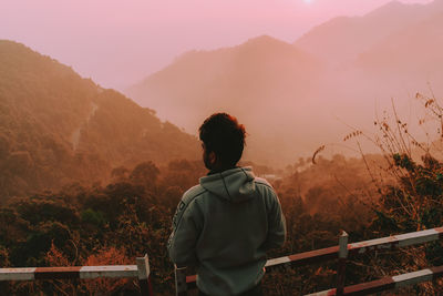 Rear view of man looking at mountains against sky