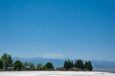 Paragliders flying above white travertines of pamukkale in an ancient city of hierapolis in turkey.