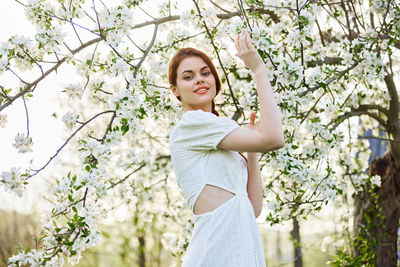 Young woman standing against cherry blossom tree