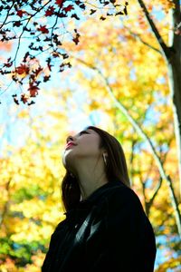 Young woman looking away while standing on tree during autumn