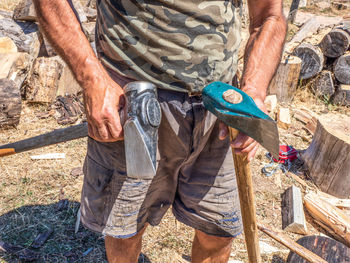 Midsection of man holding axes while standing on land