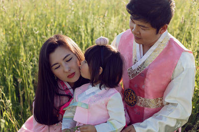 Korean family in national costumes is sitting in a field at sunset in the grass