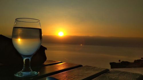 Glass on table by sea against sky during sunset