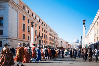 People in costume walking on street in city against clear blue sky during festival