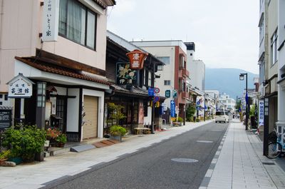 Empty road amidst buildings in city against sky