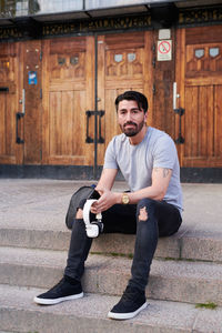 Full length of male student with headphones sitting on steps of language school