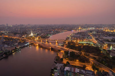 High angle view of illuminated buildings by river against sky at sunset