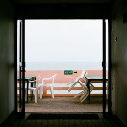 Empty chairs and tables against sky seen through window