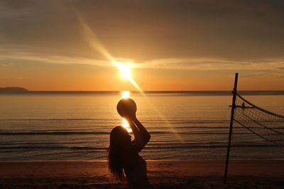 Silhouette woman playing volleyball at beach against sky during sunset