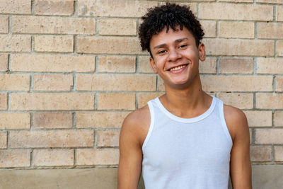 Portrait of smiling young man standing against brick wall