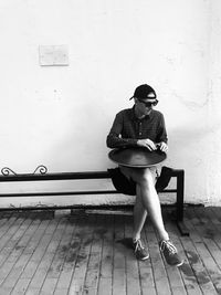 Young woman looking away while sitting on seat against wall