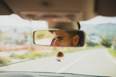 Close-up young man reflecting in rear-view mirror