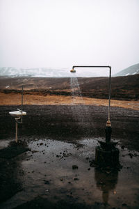 Retro shower pouring water on ground near stone hills in snow and cloudy sky