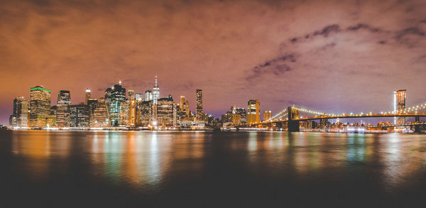 Illuminated bridge over river with buildings in background