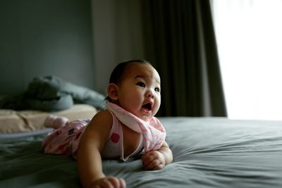 Cute toddler with mouth open lying on bed at home