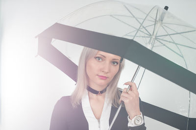 Portrait of young woman holding umbrella while standing against white background