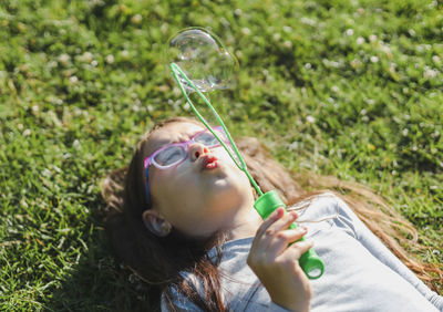 Portrait of a beautiful caucasian girl blowing soap bubbles while lying in the park.