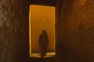 Rear view of woman walking against yellow wall