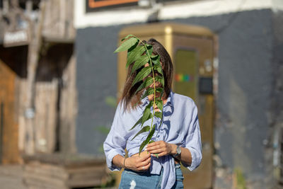 Young woman covering face with twig while standing outdoors