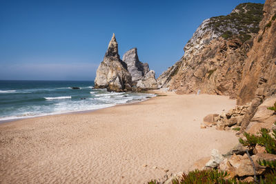 Rock formations on beach against clear blue sky