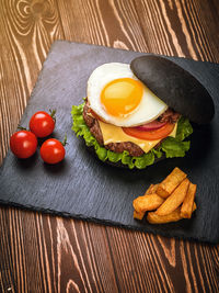 Black burger with an egg on a stone plate. cherry tomatoes. fried potatoes.