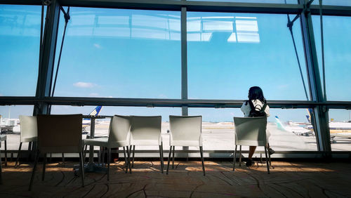 Rear view of woman sitting on chair against window