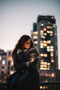 Portrait of woman standing against illuminated city at night