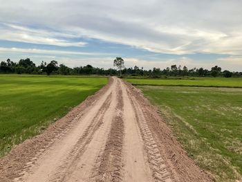 Dirt road amidst field against sky