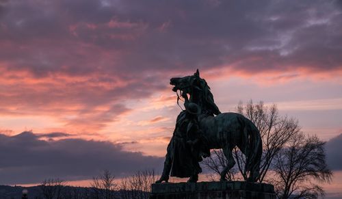 Statues against cloudy sky during sunset