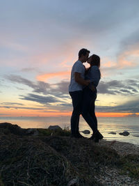 Friends standing on shore against sky during sunset