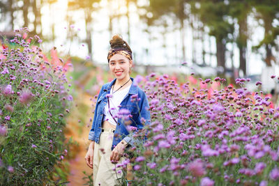 Portrait of young woman smiling while standing amidst purple flowers at park