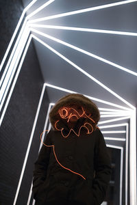 Woman in hooded clothing with light painting standing against illuminated lights