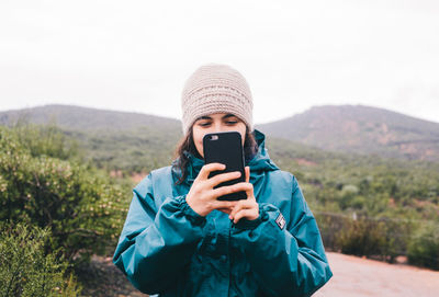 Portrait of man photographing with mobile phone against sky