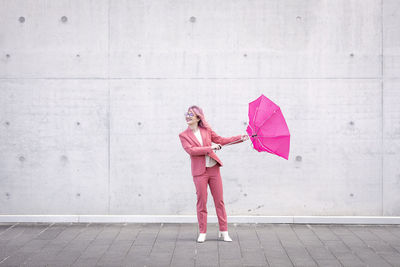 Smiling woman holding umbrella in front of wall