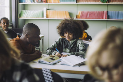 Male teacher assisting boy studying at desk in classroom