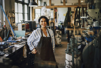Smiling female business owner leaning on chair at workshop