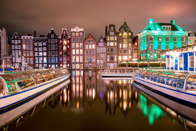 Buildings in city by river against cloudy sky