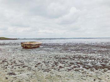 Fishing boat moored at beach against cloudy sky