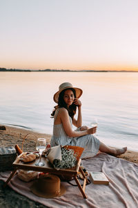 Portrait of woman sitting in hat against sky during sunset