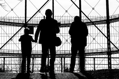 Silhouette people standing by fence